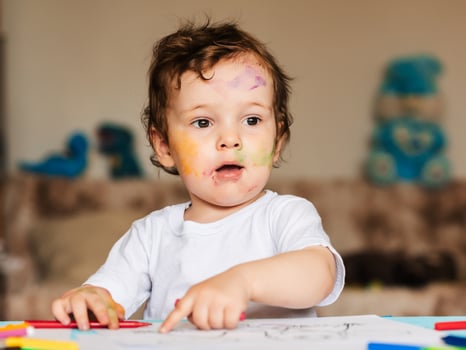 Happy little boy draws with colored pencils in an album photo