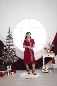 Portrait of a pretty young girl wearing a red gown, smiling at the camera, standing in decorated Christmas living room indoors photo