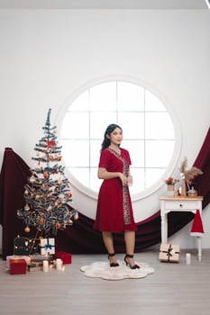 Portrait of a pretty young girl wearing a red gown, smiling at the camera, standing in decorated Christmas living room indoors photo