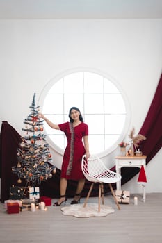 Portrait of a pretty young girl wearing a red gown, smiling at the camera, standing in decorated Christmas living room indoors photo