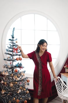 Portrait of a pretty young girl wearing a red gown, smiling at the camera, standing in decorated Christmas living room indoors photo
