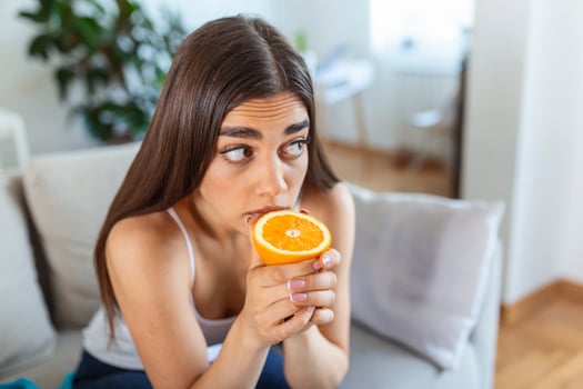 Sick woman trying to sense smell of half fresh orange, has symptoms of Covid-19, corona virus infection - loss of smell and taste. One of the main signs of the disease. photo