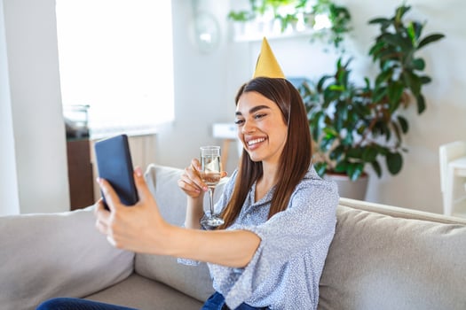Virtual Party. Happy young woman in hat having video conference online meeting with friends and family, holding glass of wine, toasting and celebrating birthday, staying at home photo
