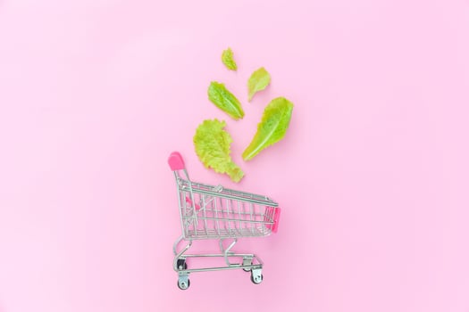Ecology eco products health food vegan vegetarian concept . Small supermarket grocery push cart for shopping with green lettuce leaves isolated on pink pastel colorful background. Copy space. photo