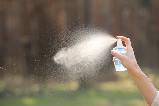 Woman hand holding a bottle and spraying on nature background. antiseptic, mosquito repellent, freshening the air photo