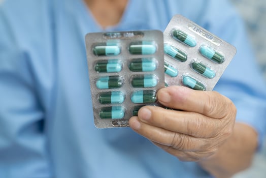 Asian senior or elderly old lady woman patient holding antibiotics capsule pills in blister packaging for treatment infection patient in hospital, Pharmacy drugstore concept. photo