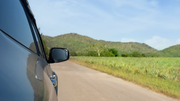 Abstract beside surface of gray car can view mirror wing of car driveing on the asphalt road. beside with blurred of pineapple plantation and distant mountains under blue sky. photo