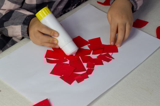 Little girl making red heart applique with paper and glue on white sheet,Valentines Day greeting card, holiday gift for Mothers day,hand made kids present,love symbol with paper,toddler activity photo