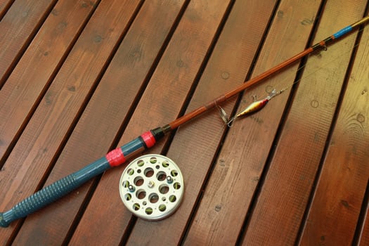 vintage fishing rod with a big reel and a wobbler on a wooden background photo