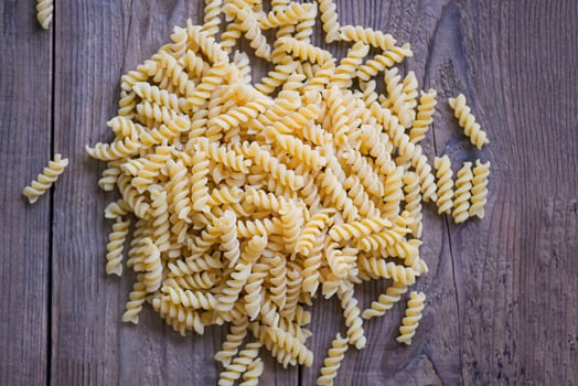Raw pasta macaroni on wooden background, close up raw macaroni spiral pasta uncooked delicious fusilli pasta for cooking food photo