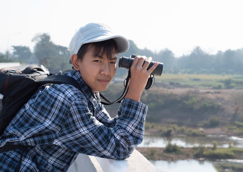 Asian boy is using binoculars to do the birds' watching in tropical forest during summer camp, idea for learning creatures and wildlife animals and insects outside the classroom. photo