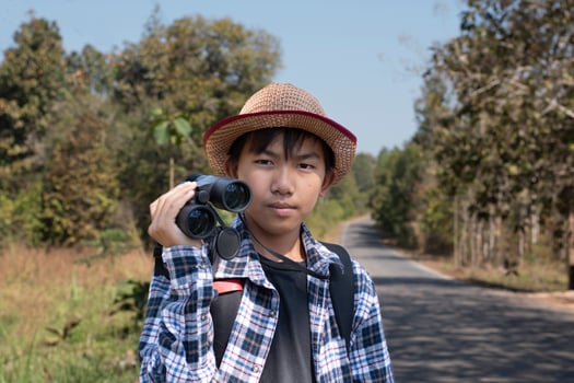 Asian boy is using binoculars to do the birds' watching in tropical forest during summer camp, idea for learning creatures and wildlife animals and insects outside the classroom. photo