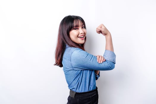 Excited Asian woman wearing a blue shirt showing strong gesture by lifting her arms and muscles smiling proudly photo