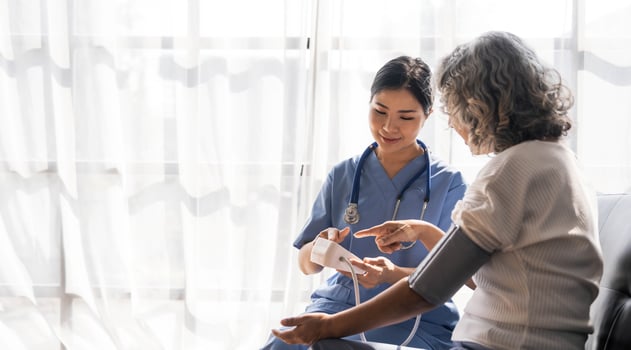 Happy senior woman having her blood pressure measured in a nursing home by her caregiver. Happy nurse measuring blood pressure of a senior woman in living room photo