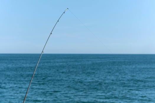 Fishing rod against blue ocean or sea background, copy space. Waiting for biggest haul. Meditative relax sport. photo