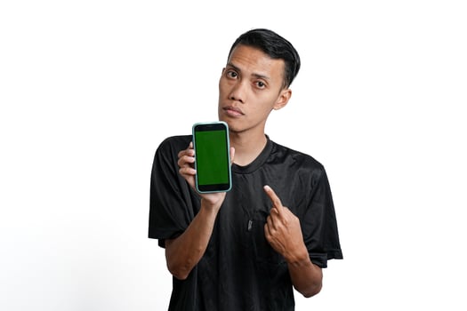 excited asian man wearing black workout t-shirt, pointing at green screen of smartphone. Isolated by white background photo