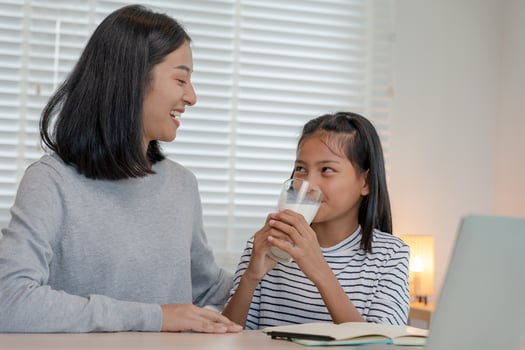 Asian young little girl learn at home. Do homework with kind mother help, encourage for exam. Mom pass on a glass of milk to daughter. Girl happy Homeschool. Mom teach and advice education together. photo