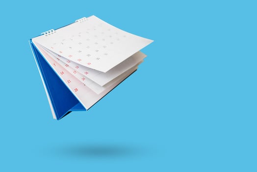 White paper desk calendar flipping page isolated on blue background photo