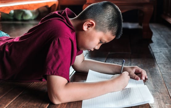 Close-up of an Asian boy sitting on the wooden floor writing a book or doing homework with a very determined face at home. photo