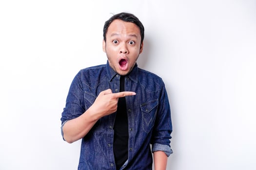 Shocked Asian man wearing blue shirt pointing at the copy space beside him, isolated by white background photo