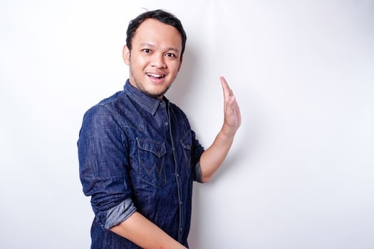 Excited Asian man wearing blue shirt pointing at the copy space beside him, isolated by white background photo