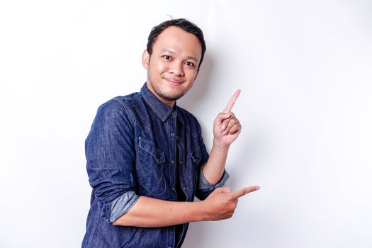 Excited Asian man wearing blue shirt pointing at the copy space beside him, isolated by white background photo