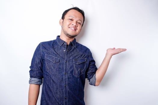 Excited Asian man wearing blue shirt pointing at the copy space beside him, isolated by white background photo
