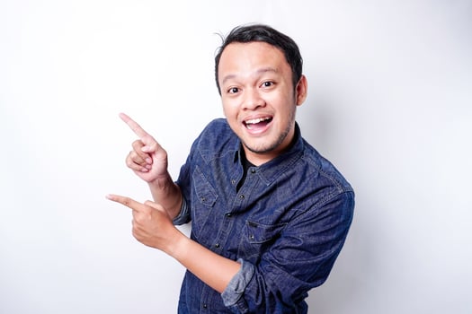 Excited Asian man wearing blue shirt pointing at the copy space beside him, isolated by white background photo