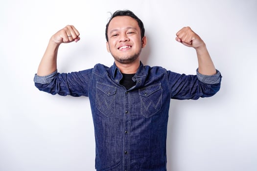 Excited Asian man wearing a blue shirt showing strong gesture by lifting his arms and muscles smiling proudly photo