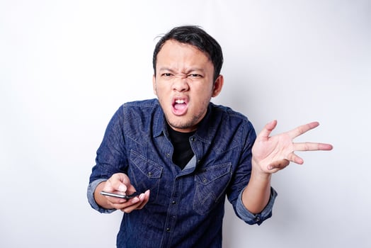 The angry and mad face of Asian man in blue shirt holding his phone isolated white background. photo