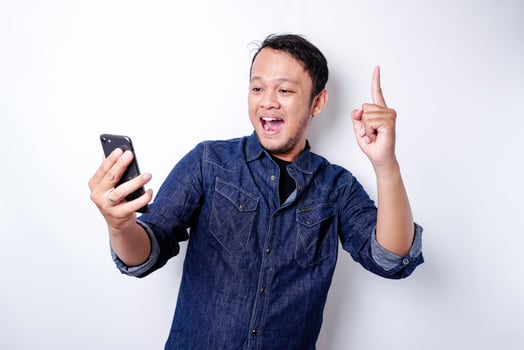 A portrait of a happy Asian man wearing a blue shirt and holding her phone, isolated by white background photo