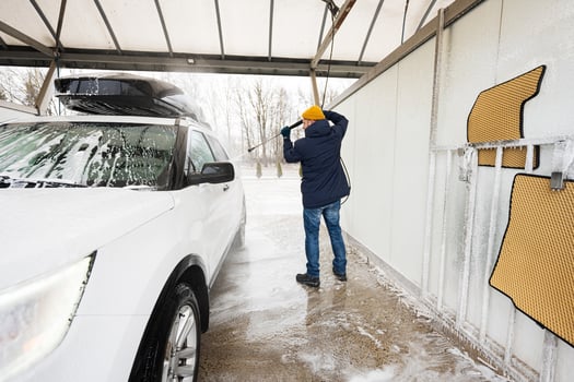 Man washing high pressure water american SUV car with roof rack at self service wash in cold weather. photo