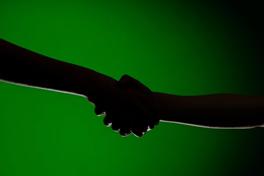 Two hands handshake, isolated on a green background, symbolizing friendship and reconciliation photo