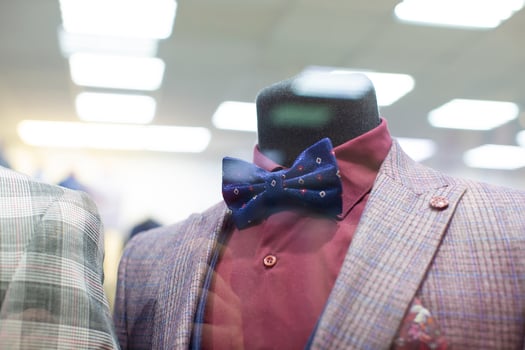 In the shop window is a mannequin in a formal suit and bow tie. photo