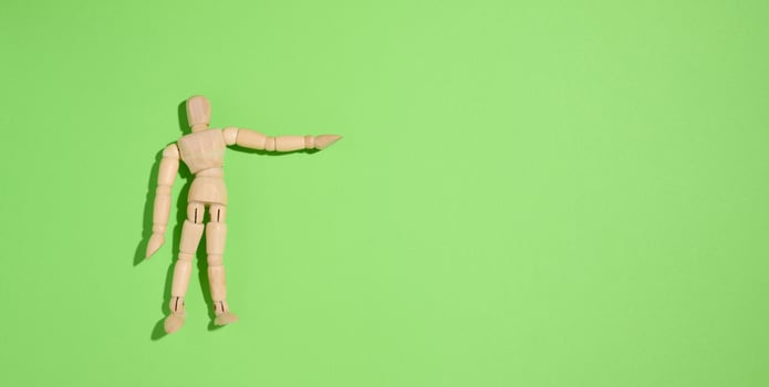 Wooden puppet man on a green background, pointing with his hand photo