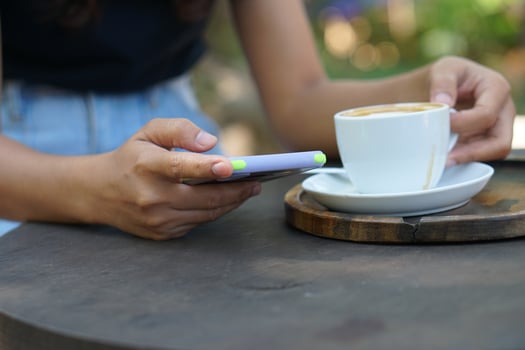 Asian woman looking at earnings on her phone at a coffee shop where she can go to work. amidst green nature photo