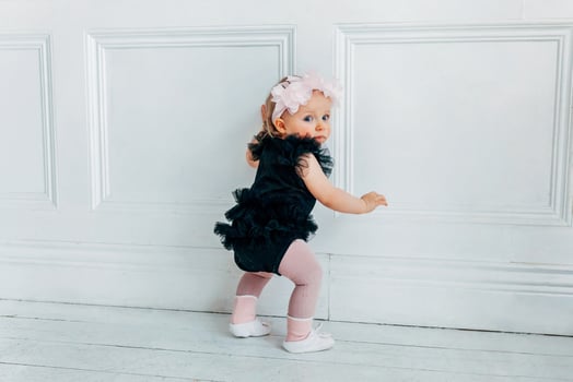 Little crawling baby girl one year old standing on floor in bright light living room smiling and laughing photo