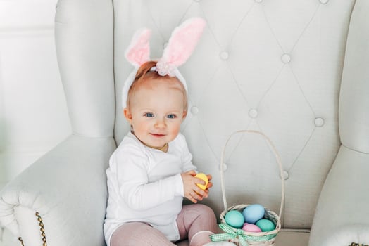 Little child girl wearing bunny ears on Easter day and playing with painted eggs photo