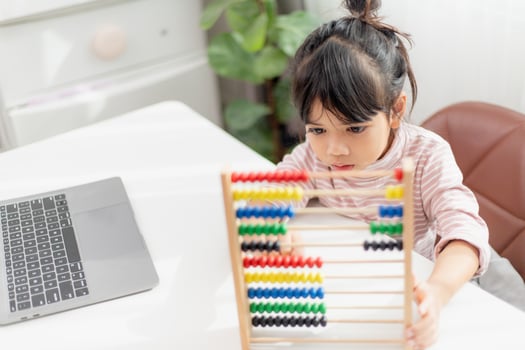 A young cute Asian girl is using the abacus with colored beads to learn how to count at home photo