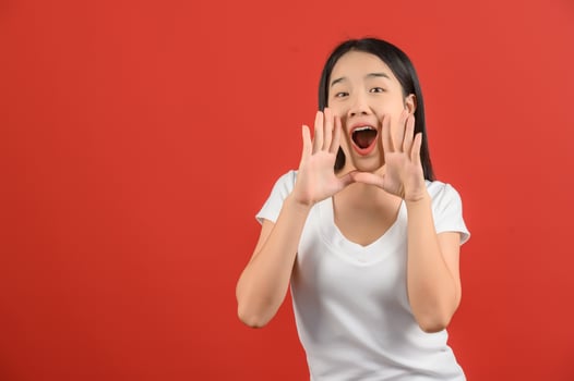 portrait of Young asian woman in white t-shirt shout story or making announcement isolated on red background photo