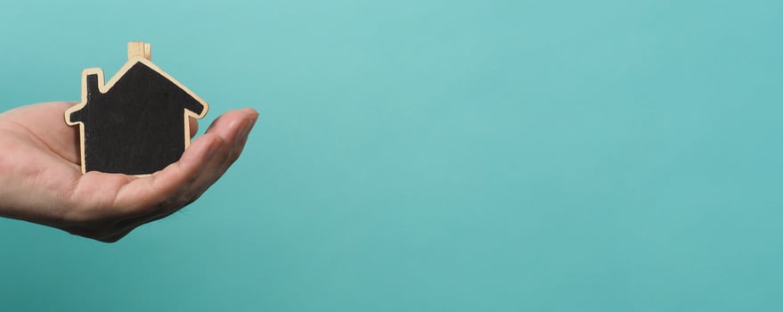 Small wood house in hands represent concepts such as home care family love real estate housing shelter insurance and mortgage. Hands holding small model house isolated on blue green studio background. photo