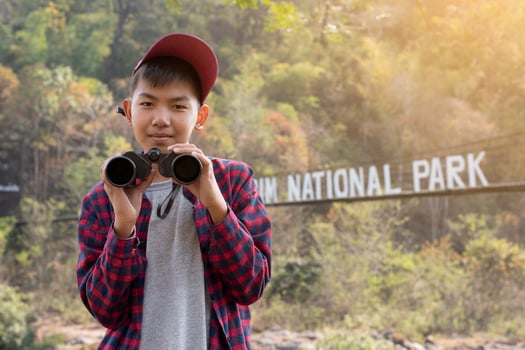 Asian boys using binoculars to watch birds on trees and fish in river in local national park during summer camp, idea for learning creatures and wildlife animals and insects outside the classroom. photo