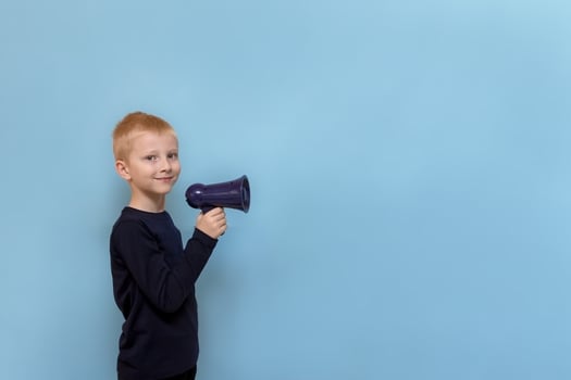 cute blond boy with megaphone smiling on blue background with copy space photo