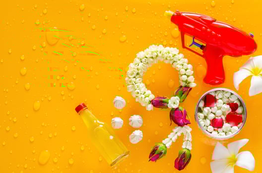 Songkran festival background with jasmine garland, water gun, flowers in water bowl, scented water and marly limestone put on clear mirror that have wet yellow background below. photo