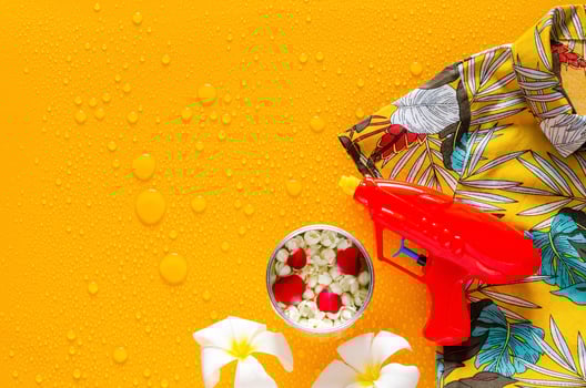 Songkran festival background with colorful shirt, water gun, flowers in water bowl and jasmine garland put on clear mirror that have wet yellow background below. photo
