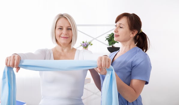 Physiotherapist and woman sitting on a bed exercising with a rubber tape photo