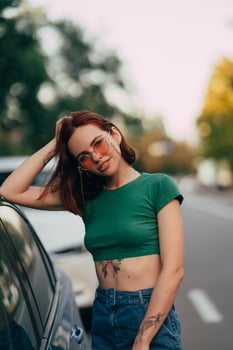 Beautiful fashionable young woman in glasses posing near car photo