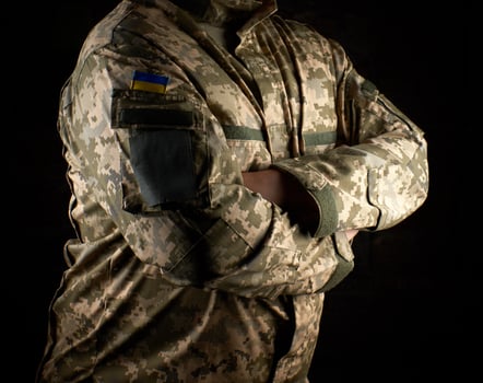 Ukrainian soldier in camouflage uniform stands with arms crossed on his chest photo