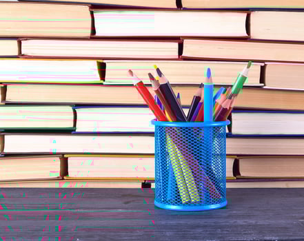 various hardback books and blue stationery glass with multi-colored wooden pencils photo