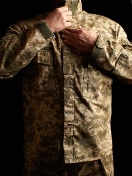 Ukrainian soldier dressed in uniform stands in the dark and fastens his jacket photo